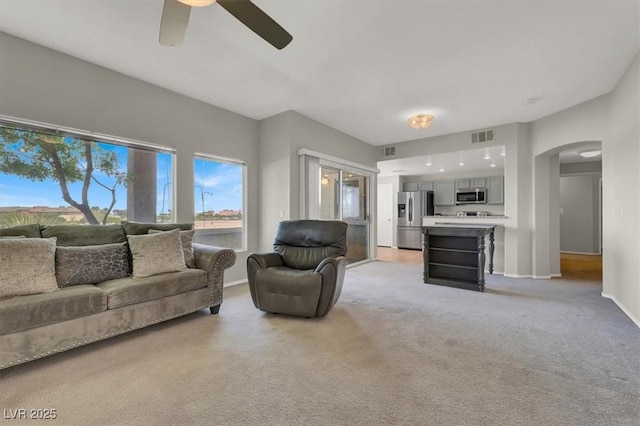 living area with light carpet, arched walkways, visible vents, baseboards, and a ceiling fan