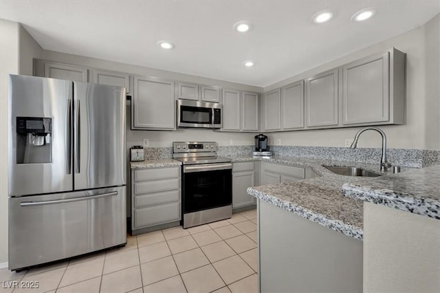 kitchen with light stone counters, a sink, light tile patterned flooring, gray cabinets, and appliances with stainless steel finishes