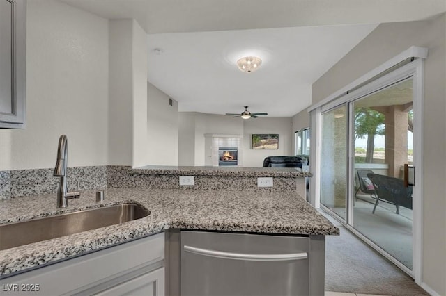 kitchen featuring a ceiling fan, a sink, dishwasher, carpet floors, and light stone countertops