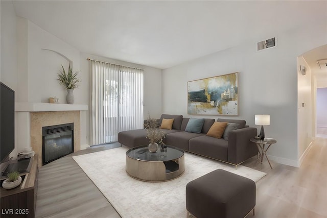 living area featuring baseboards, a glass covered fireplace, visible vents, and light wood-type flooring