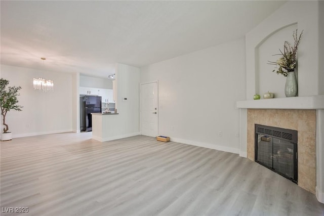 unfurnished living room featuring light wood-type flooring, a tile fireplace, baseboards, and a chandelier