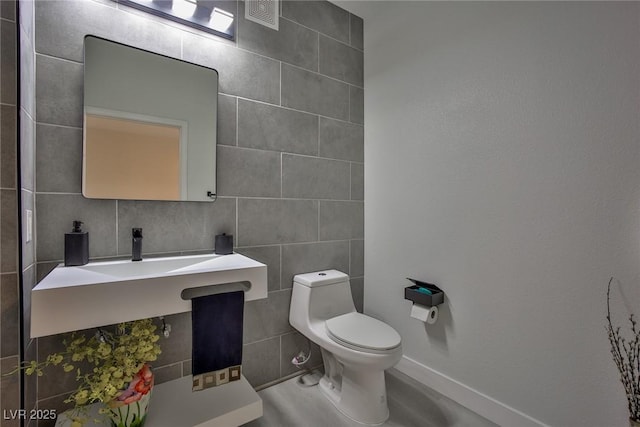 half bath with visible vents, tile walls, baseboards, and toilet