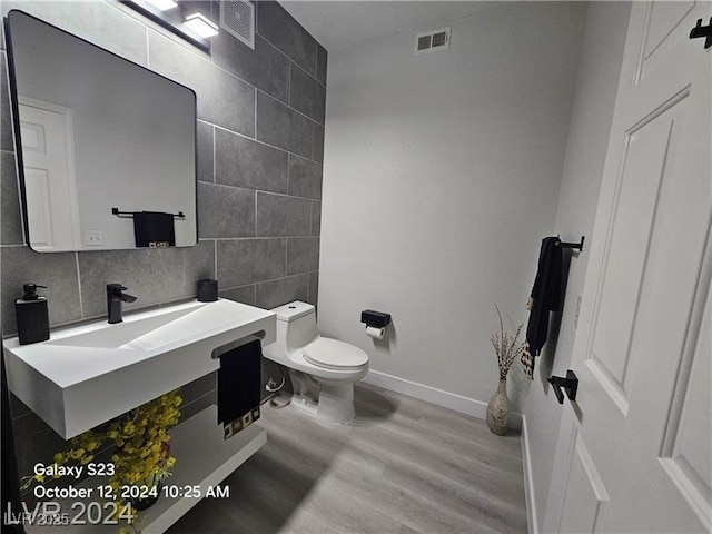 bathroom featuring toilet, wood finished floors, tile walls, baseboards, and visible vents