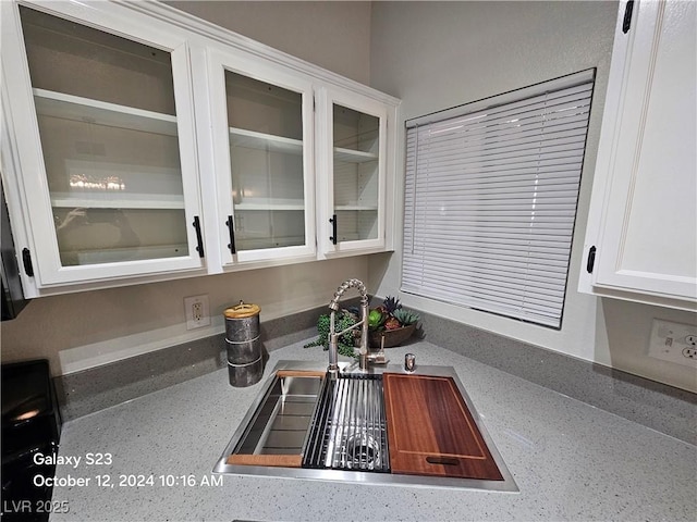 room details with white cabinets, glass insert cabinets, a sink, and light stone counters