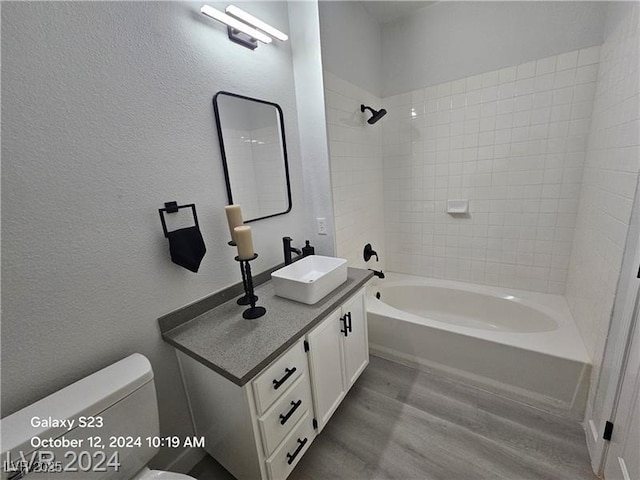 bathroom with toilet, shower / bathtub combination, wood finished floors, a textured wall, and vanity
