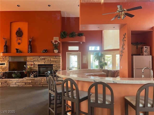 kitchen featuring a stone fireplace, tile countertops, freestanding refrigerator, carpet flooring, and open floor plan