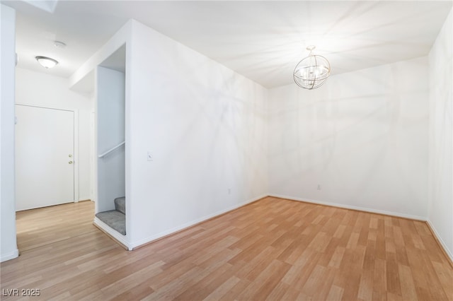 unfurnished room with baseboards, wood finished floors, an inviting chandelier, and stairs