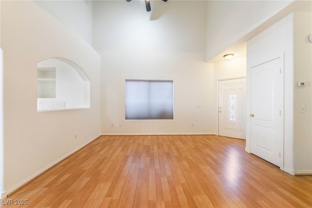 interior space with light wood-type flooring, a high ceiling, a ceiling fan, and baseboards