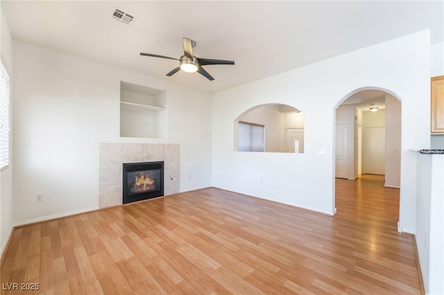 unfurnished living room with light wood-style flooring, visible vents, built in shelves, a ceiling fan, and a tile fireplace