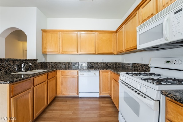 kitchen with a peninsula, a sink, dark stone counters, light wood-style floors, and white appliances