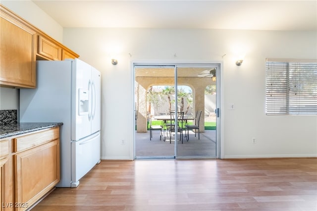 kitchen featuring stone counters, baseboards, white fridge with ice dispenser, and light wood-type flooring