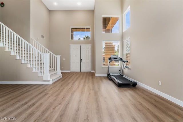 foyer entrance featuring a towering ceiling, wood finished floors, stairs, and baseboards