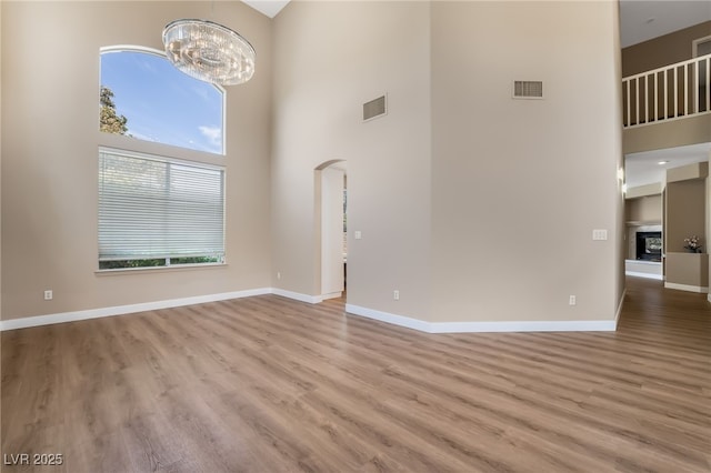 unfurnished living room featuring a high ceiling, a notable chandelier, wood finished floors, and visible vents