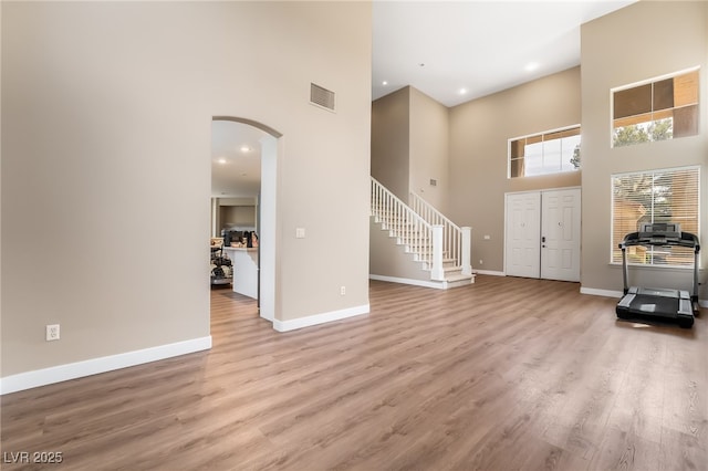 foyer entrance featuring arched walkways, baseboards, visible vents, a high ceiling, and stairs