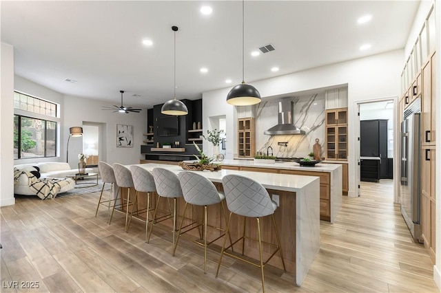 1350 Rossini St, Henderson, NV 89052 - kitchen with wall chimney range hood, a spacious island, high end refrigerator, light wood finished floors, and recessed lighting