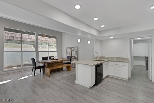 kitchen featuring a peninsula, dishwasher, light wood-style flooring, and a sink