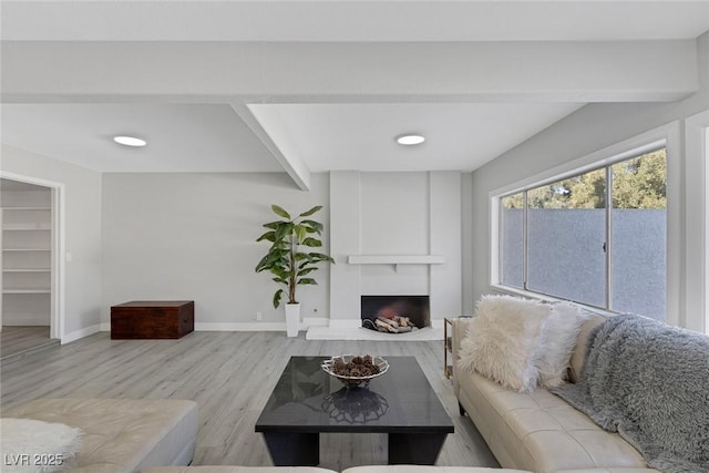 living area with baseboards, a large fireplace, wood finished floors, and beam ceiling
