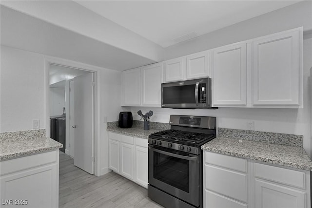 kitchen with white cabinets, light wood-type flooring, appliances with stainless steel finishes, and light stone counters