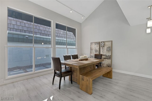 dining area with track lighting, baseboards, wood finished floors, and high vaulted ceiling