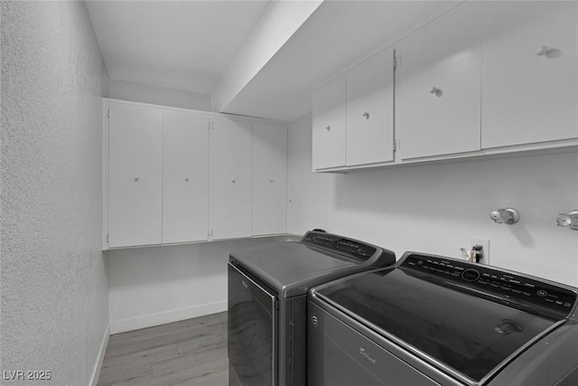 clothes washing area with cabinet space, a textured wall, light wood-style flooring, baseboards, and independent washer and dryer