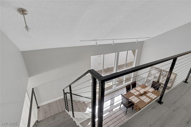 stairway with track lighting, baseboards, wood finished floors, and a textured ceiling