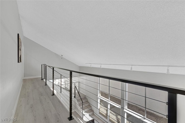 corridor featuring light wood-style flooring, a textured ceiling, baseboards, and an upstairs landing