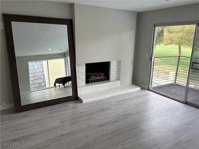 unfurnished living room featuring baseboards, a fireplace, wood finished floors, and a wealth of natural light