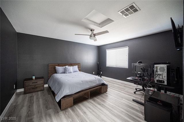 bedroom featuring wood finished floors, visible vents, a ceiling fan, baseboards, and attic access