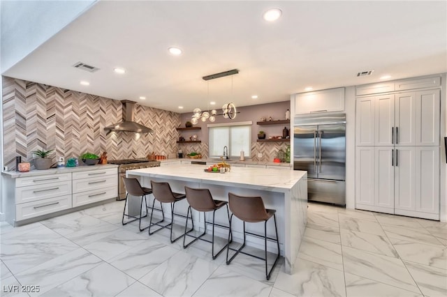 kitchen with high quality appliances, open shelves, light stone countertops, wall chimney exhaust hood, and visible vents