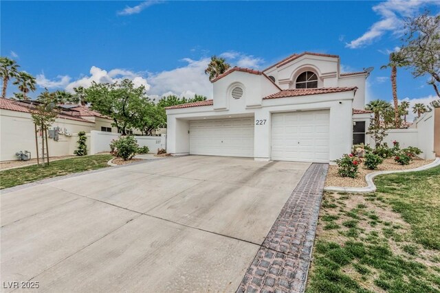 mediterranean / spanish-style home with stucco siding, a tile roof, concrete driveway, and fence