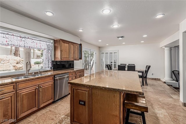kitchen with ornate columns, dishwasher, a sink, dark stone counters, and a breakfast bar area