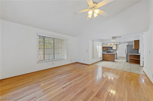 unfurnished living room with high vaulted ceiling, light wood finished floors, baseboards, and ceiling fan