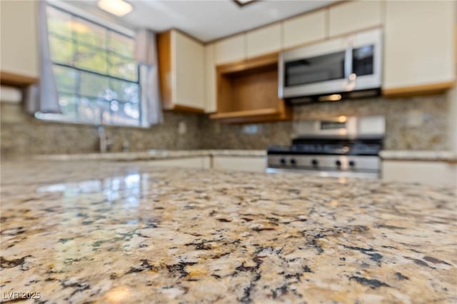 kitchen with tasteful backsplash, light stone countertops, stove, and white microwave