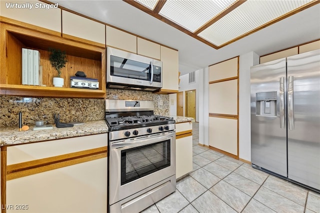 kitchen with tasteful backsplash, light tile patterned flooring, stainless steel appliances, light stone countertops, and visible vents