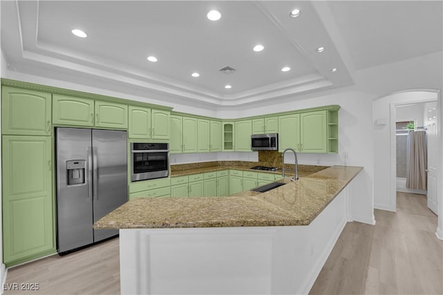 4722 Blue Mesa Way, Las Vegas, NV 89129 - kitchen with appliances with stainless steel finishes, a tray ceiling, a peninsula, arched walkways, and stone countertops
