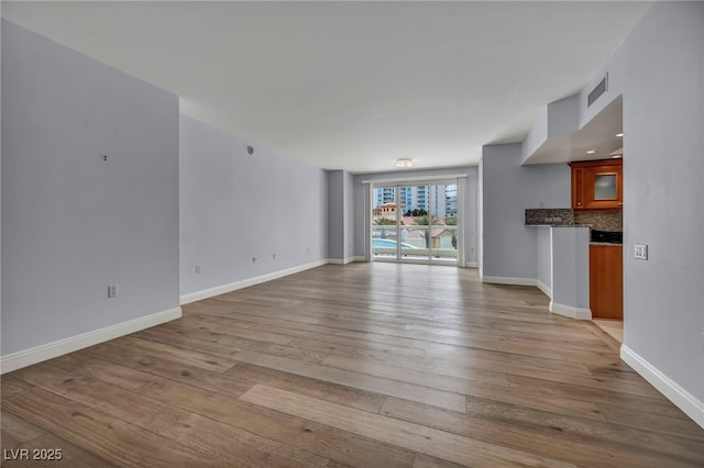 unfurnished living room featuring wood-type flooring, baseboards, and visible vents