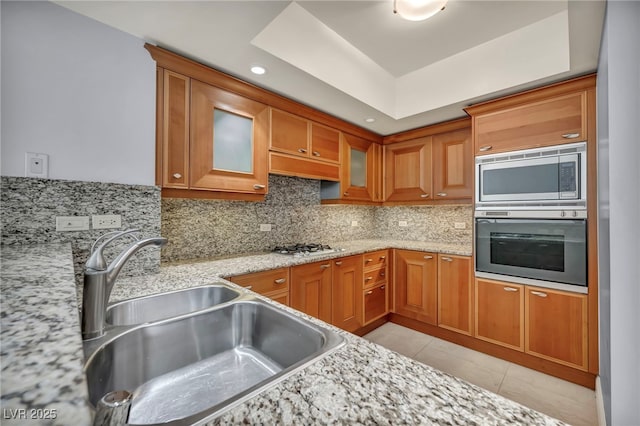 kitchen with decorative backsplash, brown cabinets, a sink, light tile patterned floors, and stainless steel appliances