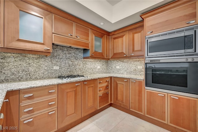 kitchen featuring tasteful backsplash, stainless steel microwave, wall oven, and light stone countertops