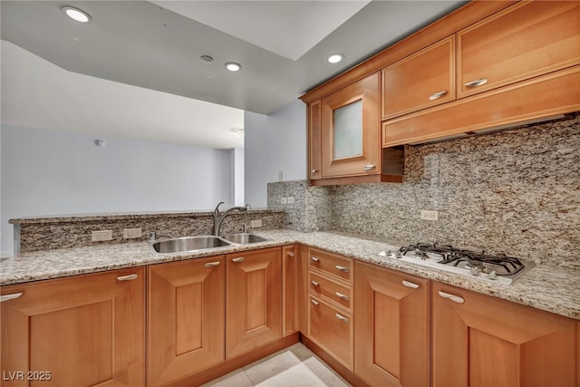 kitchen with white gas stovetop, backsplash, light stone countertops, and a sink