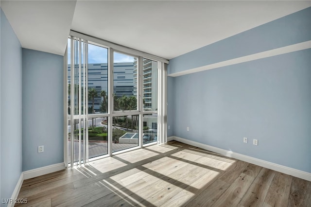 empty room featuring baseboards, wood finished floors, and a wall of windows