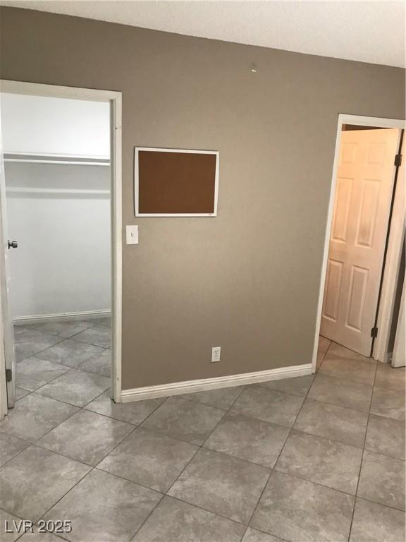 unfurnished bedroom with baseboards, tile patterned flooring, a closet, and a walk in closet