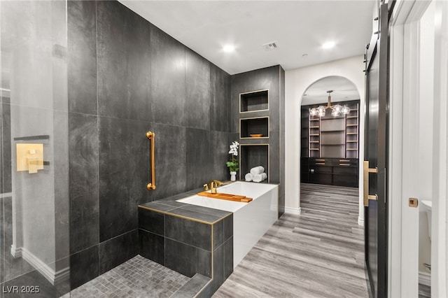 bathroom with wood finished floors, a walk in closet, a tub, visible vents, and tiled shower