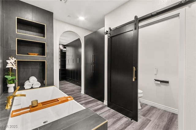 bathroom with a bath, toilet, baseboards, visible vents, and wood finished floors