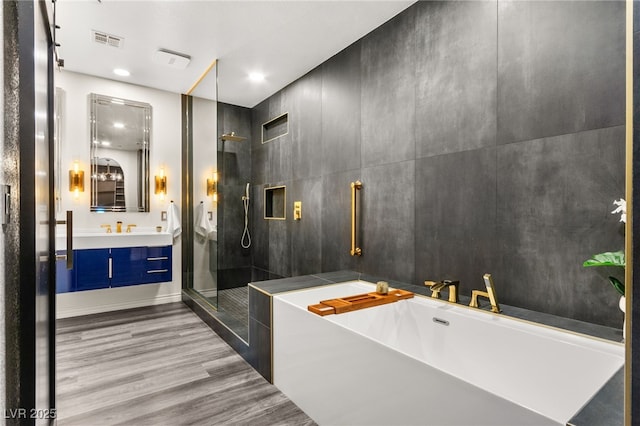 full bath featuring a shower stall, a freestanding bath, wood finished floors, visible vents, and vanity