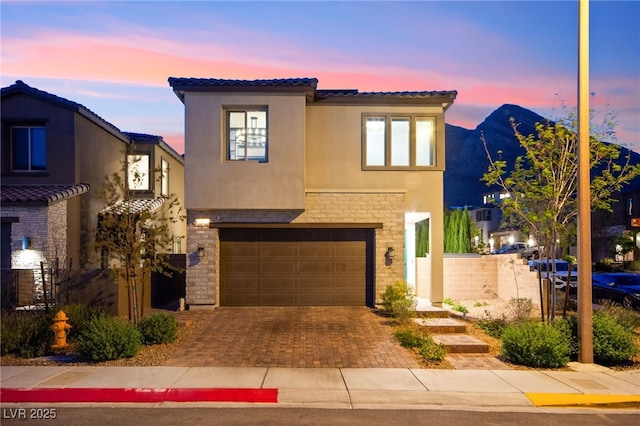 view of front of home featuring a tiled roof, stucco siding, an attached garage, decorative driveway, and stone siding
