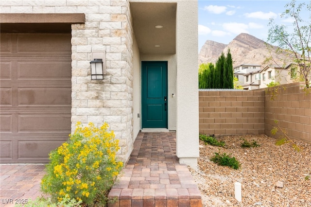 entrance to property with a garage, stone siding, and fence