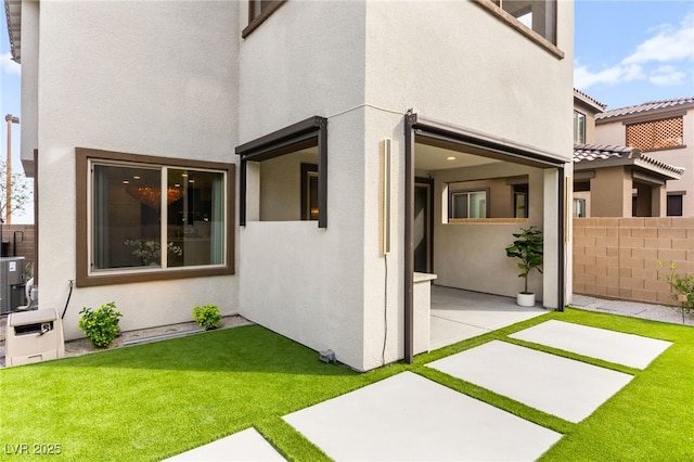 entrance to property with fence, a patio, a yard, and stucco siding