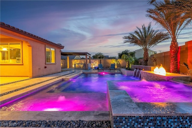 pool at dusk with a fire pit, a fenced backyard, and a pool with connected hot tub