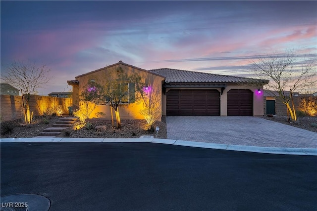 view of front of house featuring a garage, a tiled roof, stucco siding, decorative driveway, and fence