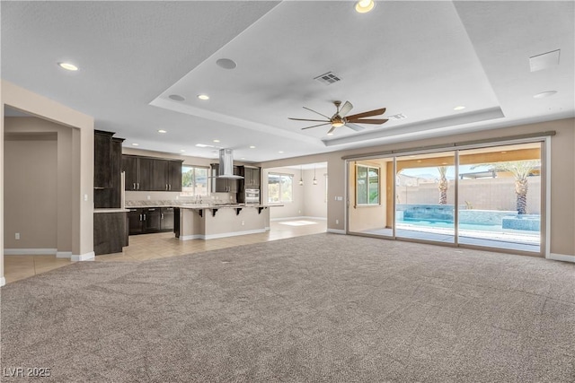 unfurnished living room featuring a tray ceiling, ceiling fan, light colored carpet, recessed lighting, and baseboards